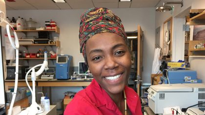 Person smiling with lab equipment in background.