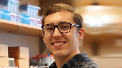 Person with glasses and brown hair in front of lab shelves