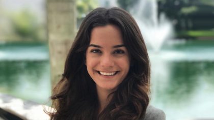 Person with shoulder-length hair in front of a fountain on a pond.