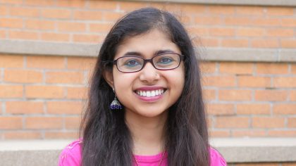 Person with long hair and glasses in front of bricks