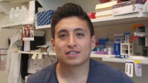 Person with black hair in front of lab shelves