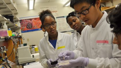 Female and male students in lab coats looking at dish