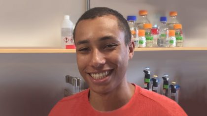 Person with short black hair in front of lab shelves