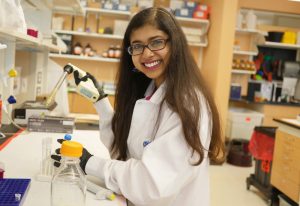 Person with long hair and glasses in lab coat pipetting