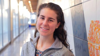 Person with long, brown hair smiling in hallway