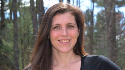 Person with brown hair smiling in woods